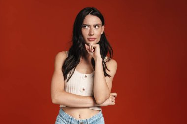 Hoş, ciddi bir kadının kırmızı arka planda izole bir şekilde düşünmesi ve bakması.