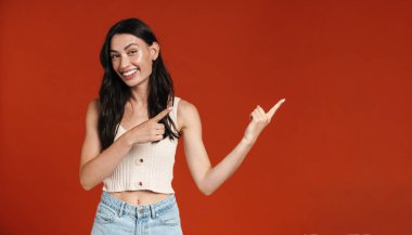 Kırmızı arka planda izole edilmiş, gülümseyen ve parmakla işaret eden genç bir kadın görüntüsü