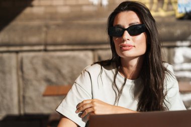 Dışarıdaki kafede dizüstü bilgisayar kullanan ciddi bir genç kadın görüntüsü