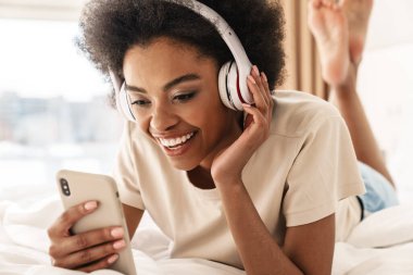 Kötü bir şekilde kulaklık ve cep telefonu kullanırken gülümseyen neşeli Afrikalı Amerikalı kız görüntüsü