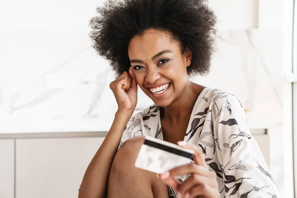 Podekscytowana Młoda Kobieta Pokazuje Kartę Kredytową Siedząc Laptopem Przy Stole — Zdjęcie stockowe
