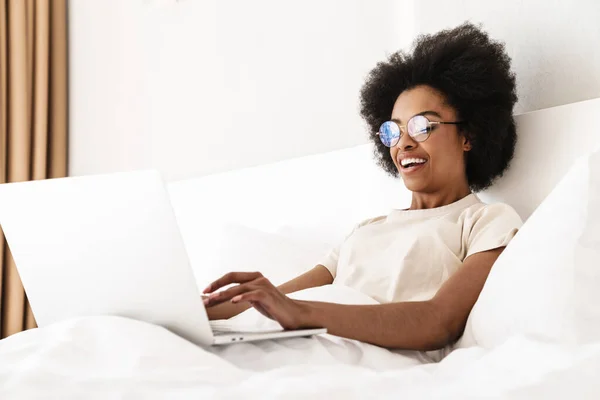 快乐的年轻非洲女人躺在床上用手提电脑和朋友们视频聊天 — 图库照片