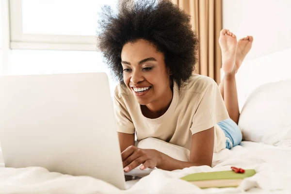 快乐的年轻非洲女人躺在床上用手提电脑和朋友们视频聊天 — 图库照片