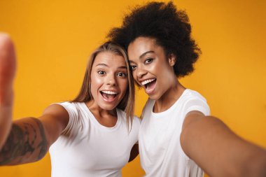 Çok ırklı genç kızların, sarı arka planda izole edilmiş kamerayla selfie çekmesine şaşıran pozitiflik.