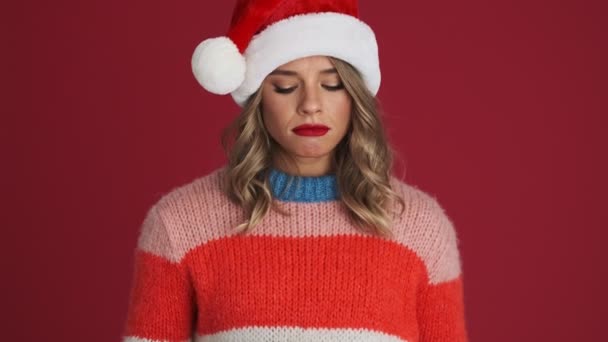 在红墙的背景下 戴着圣诞礼帽的年轻而悲伤的女人拿着礼品盒 — 图库视频影像