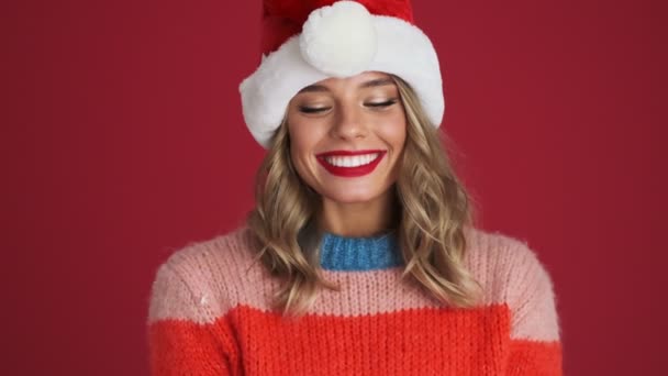 若いです正の女性でクリスマスサンタ帽子吹いオンConfetti絶縁上の赤い壁の背景 — ストック動画