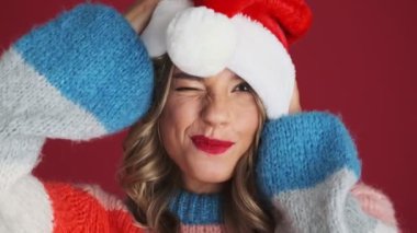 Noel Baba şapkalı neşeli iyimser kız kırmızı duvar arkasında izole edilmiş.