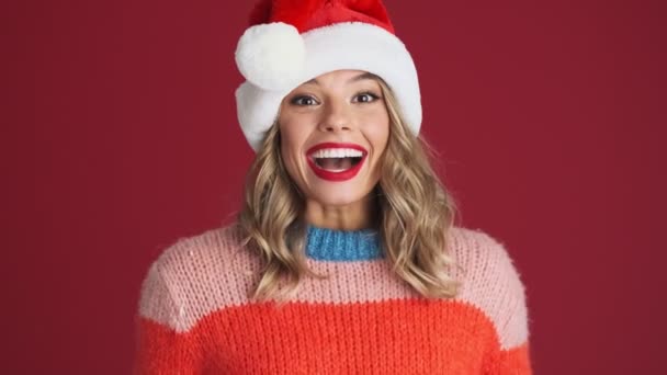 若いです正興奮可愛いです女性でクリスマスサンタ帽子クリップ彼女の手絶縁上の赤い壁の背景 — ストック動画