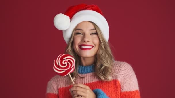 年轻快乐可爱的女人戴着圣诞礼帽 手里拿着棒棒糖 被红墙隔开了 — 图库视频影像