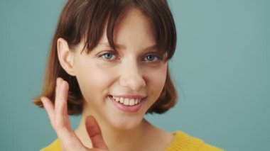 Kameraya gülümseyen bir kadının yakın çekimi stüdyonun mavi arka planında izole bir şekilde duruyor.