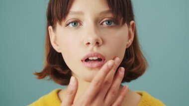 Çekici bir kadının yakın çekim görüntüsü stüdyonun mavi arka planında tek başına kameraya poz veriyor.