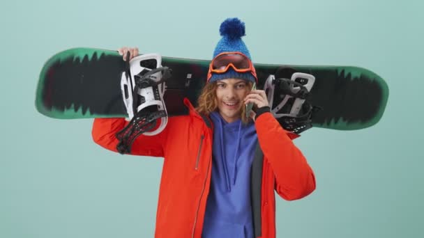 Hezký Snowboardista Mluví Telefonu Stojí Izolovaně Nad Modrým Pozadím Studiu — Stock video