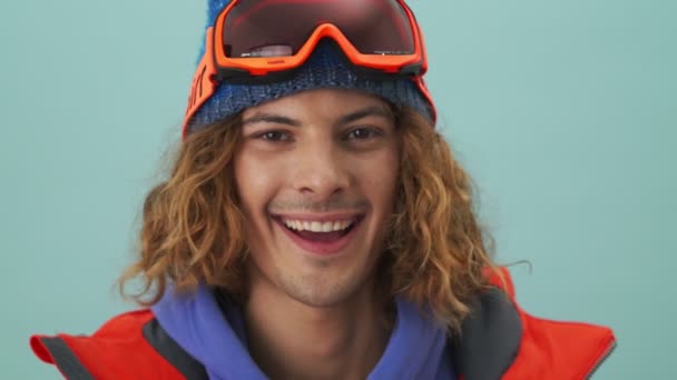 Pozitivní Snowboardista Mrká Zatímco Dívá Kameru Stojící Izolovaně Nad Modrým — Stock video