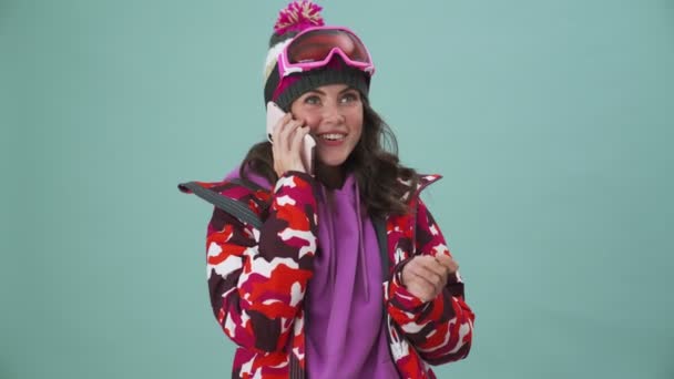 Happy Young Woman Snowboarder Talking Her Smartphone Standing Isolated Blue — Stock Video