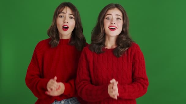 Dwie Uśmiechnięte Dziewczyny Czerwonych Swetrach Podziwiają Stojąc Samotnie Zielonym Tle — Wideo stockowe