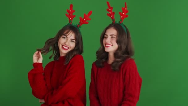 Two Smiling Girls Wearing Christmas Reindeer Antlers Red Sweaters Standing — ストック動画