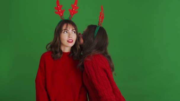 Twee Vrolijke Meisjes Met Kerstrendieren Gewei Rode Truien Delen Geheimen — Stockvideo