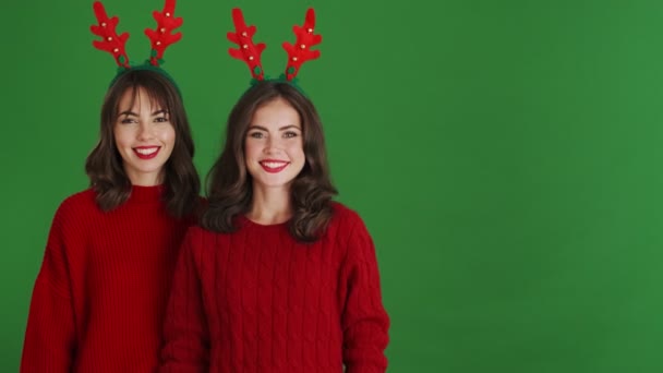 Dos Chicas Sonrientes Con Cuernos Reno Navideños Suéteres Rojos Apuntan — Vídeos de Stock