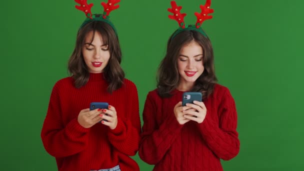 크리스마스용 사슴뿔을 스웨터를 여학생이 스튜디오의 위에서 스마트폰을 사용하고 — 비디오