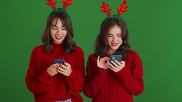 Dwie Uśmiechnięte Dziewczyny Noszące Świąteczne Rogi Reniferów Czerwone Swetry Używają — Wideo stockowe