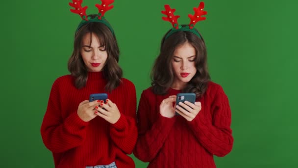 크리스마스 순록용 노래기와 스웨터를 소녀가 스튜디오 위에서 스마트폰을 사용하여 무엇인가를 — 비디오