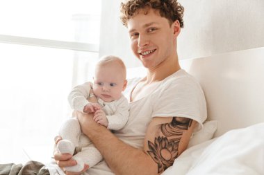 Mutlu genç baba, evde yatıp kucaklaşırken küçük oğluyla oynuyor.