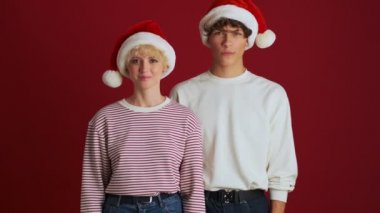 Noel Baba şapkalı kardeşiyle genç pozitif kız kırmızı duvar arkasında izole edilmiş iyi bir jest gösteriyor.