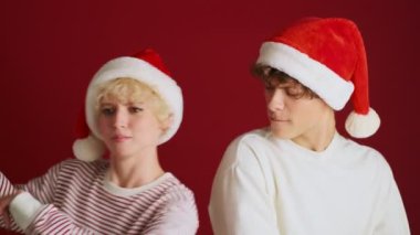 Noel Baba şapkasıyla kardeşiyle dans eden genç, mutlu bir kız. Kırmızı duvar arkasında izole edilmiş.