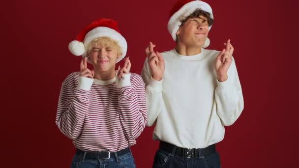 若いです願っています女の子とともに彼女の兄でクリスマスサンタ帽子作り指作る横断ジェスチャー絶縁以上赤壁の背景 — ストック動画