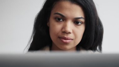 Odaklanmış bir Afrikalı Amerikalı kadının yakın plan görüntüsü bilgisayarını kapalı bir sandalyede otururken kullanıyor.