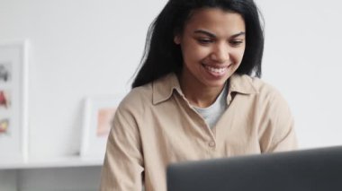 Odaklanmış bir Afrikalı Amerikalı kadının yakın plan görüntüsü bilgisayarını kapalı bir sandalyede otururken kullanıyor.