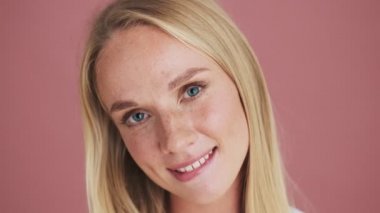 Güzel sarışın bir kadının yakın çekim görüntüsü stüdyodaki pembe arka planda tek başına duran kameraya bakıyor.
