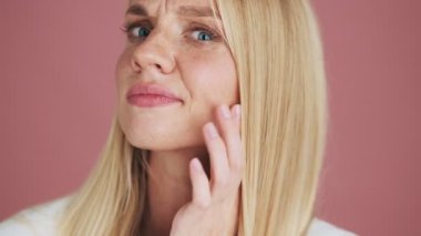 Hoşnutsuz sarışın bir kadının yakın plan görüntüsü stüdyo pembe arka planda tek başına duran yüzüne bakıyor.