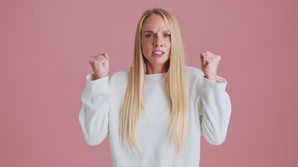 怒っているブロンド女性ありますジェスチャーとともに彼女の手と見ますザカメラスタンド絶縁上ピンクの背景でスタジオ — ストック動画