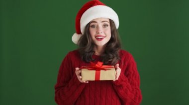 Noel Baba şapkalı mutlu kız yeşil duvar arkasında izole edilmiş hediye kutusunu tutuyor.