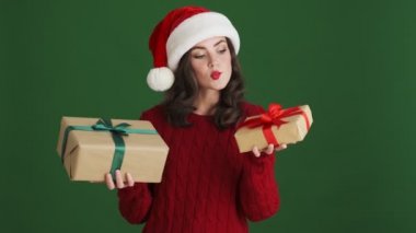 Noel Baba şapkalı kız yeşil duvar arkaplanından izole edilmiş iki hediye arasında seçim yapıyor.