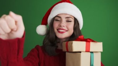 Noel Baba şapkalı neşeli kız yeşil duvar arkasında izole edilmiş hediye kutuları tutuyor.