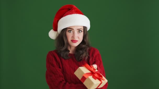 混乱ストレス女の子でクリスマスサンタ帽子保持現在のボックス孤立以上緑の壁の背景 — ストック動画