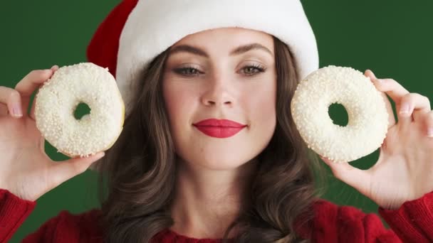 Positive Pleased Girl Christmas Santa Hat Holding Donuts Isolated Green — Stock Video