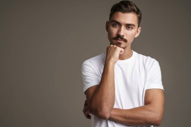 Gri arka planda kollarını çapraz yapmış, kameraya poz veren beyaz bir adam.