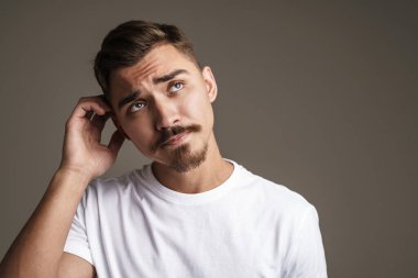 Düşünceli, tıraşsız, düşünen ve yukarı bakan adamın görüntüsü gri arka planda izole edilmiş.