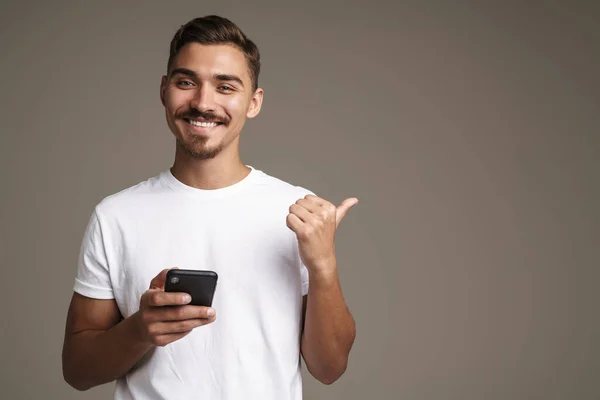 Image Joyful Unshaven Guy Pointing Finger Aside While Using Cellphone — Stock Photo, Image