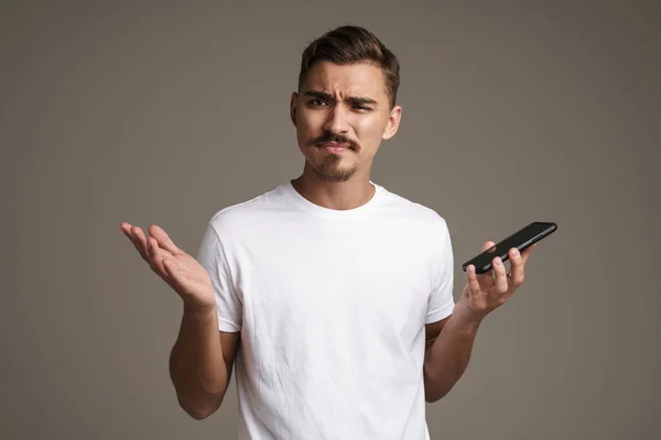 Imagen Hombre Confundido Mostrando Gestos Mientras Sostiene Teléfono Celular Aislado — Foto de Stock