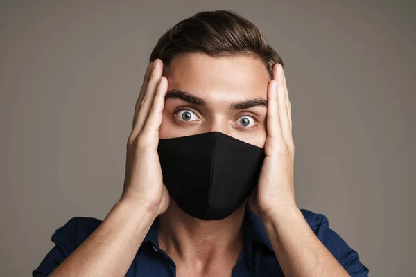 Image of shocked caucasian guy in face mask grabbing his head isolated over grey background