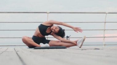 Genç, konsantre olmuş Afrikalı spor kadını sahilde esneme egzersizi yapıyor.