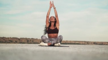 Güzel, genç, Afro-Amerikalı, gözleri kapalı spor giyimli bir kadın, dışarıda plajda minderde yoga yapıyor.