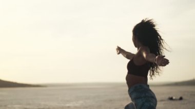 Spor giysili Afro-Amerikan bir kadın sabahleyin plajda yoga pozu veriyor.