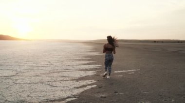 Spor giyimli, çekici, Afro-Amerikan bir kadının arkadan görünüşü sabah plajda koşuyor.