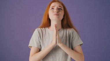 Duygusal genç bir kadın, menekşe arkaplan üzerinde izole bir şekilde dua etmek için bir şeyler istiyor.