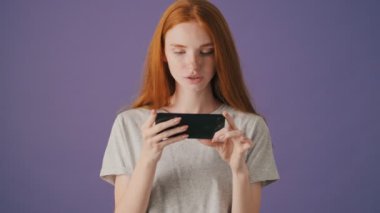 Yoğunlaşmış genç bir kadın, menekşe arka planında izole bir şekilde duran akıllı telefonuyla video izliyor.